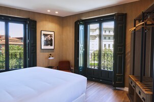 Ein Hotelzimmer mit einem großen Bett, einem Schreibtisch, einem Stuhl und einem Fenster mit Blick auf Gebäude und Grünflächen.