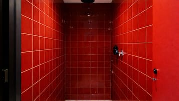A red-tiled shower stall with a ceiling-mounted showerhead and a visible drain.