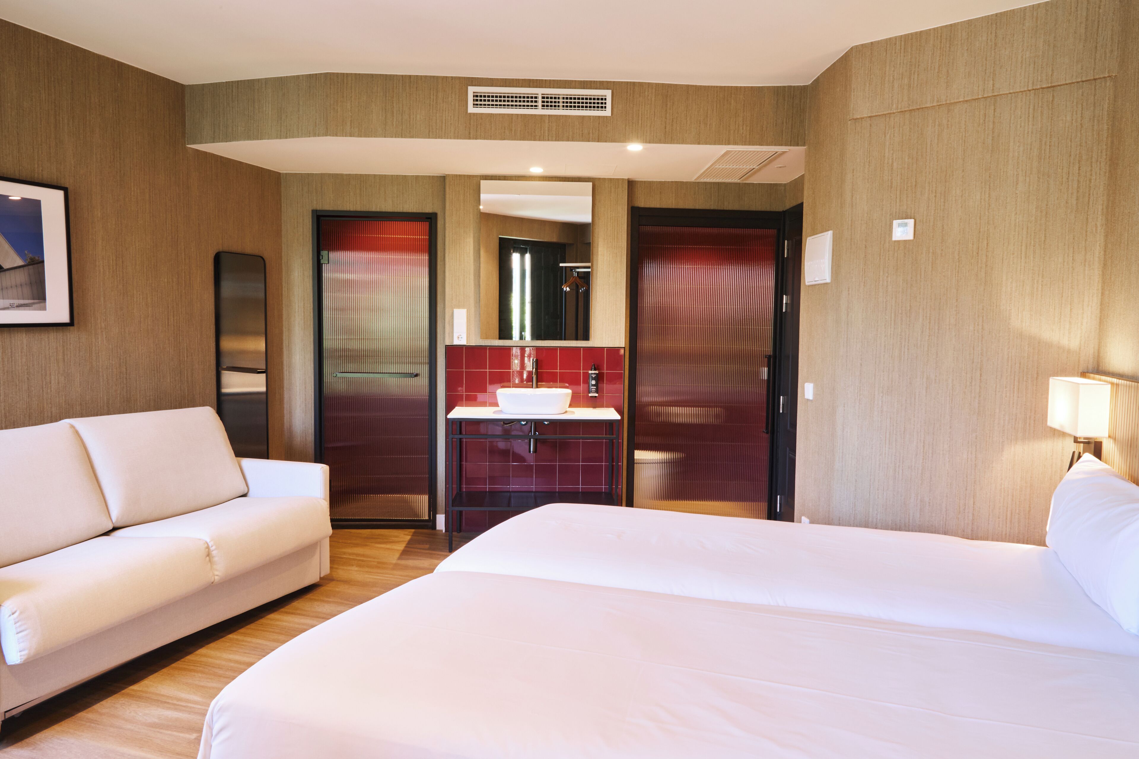A hotel room with a bed, a sofa, a bathroom with a sink, and a mirror.