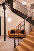 Eine Treppe mit Holzstufen und einem schwarzen Geländer, ein Ledersofa und eine Säule mit aufwendigen Schnitzereien.