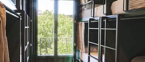 A train compartment with bunk beds, a wooden floor, and a large window with a view of trees.