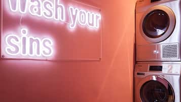 A laundry area with a neon sign that reads "Wash your sins" and a bench.