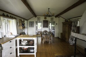 Eine traditionelle Küche mit Holzbalken, einem zentralen Holztisch und einem weißen Schrank mit Geschirr.