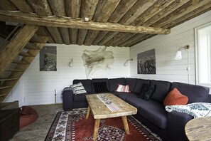 Ein Zimmer im Dachgeschoss mit Holzbalkendecke, einem dunklen Sofa, einem Holztisch und einem gemusterten Teppich.