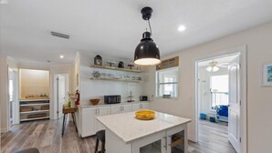 Una cocina con armarios blancos, una isla central, una lámpara colgante y vistas al área de estar contigua.