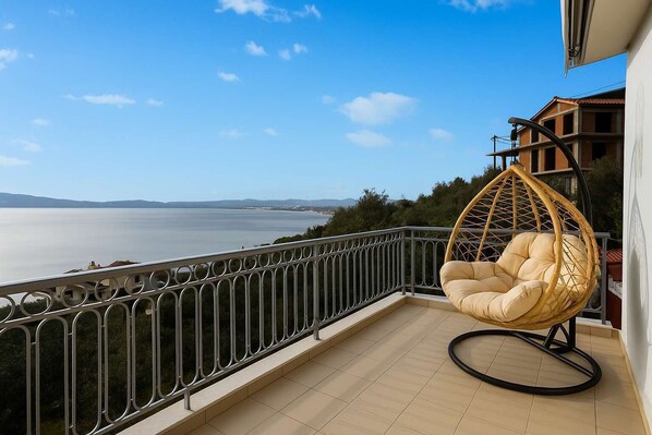 A balcony with a hanging chair overlooking a body of water and distant hills.