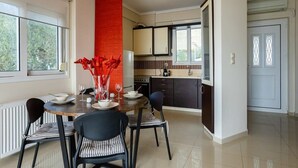 Une cuisine moderne avec un coin repas, comprenant un îlot central, des meubles de couleur sombre et un mur d’accent rouge.