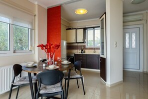 A modern kitchen with dark cabinets, a central island, and a dining area with striped chairs and a round table.