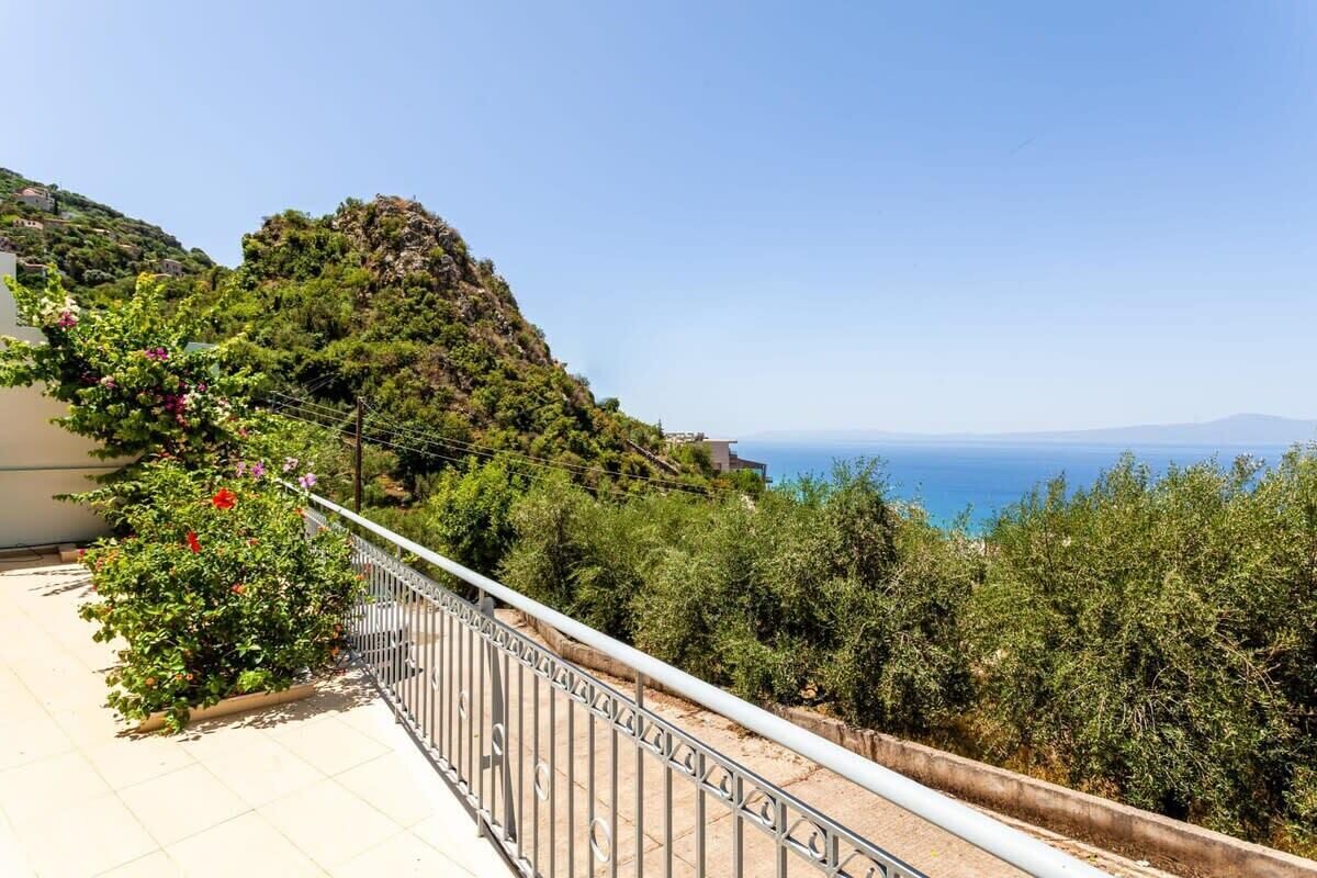 Ein Balkon mit Metallgeländer, der auf eine Küstenlandschaft mit Bäumen und Meerblick blickt.