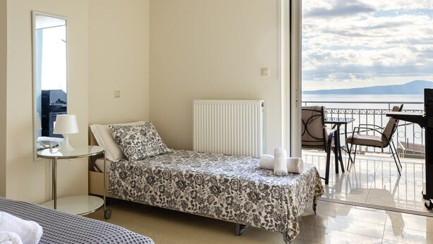 Un lit simple avec une couvre-lit à motifs floraux, une table de chevet avec une lampe, et une vue sur la mer depuis un balcon.