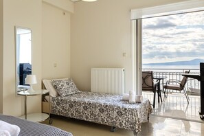 Una cama individual con cubrecama floral, una mesita de noche con lámpara y vistas al mar desde un balcón.