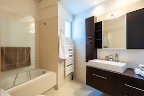 A modern bathroom with a bathtub, a large mirror, and dark wooden cabinets.