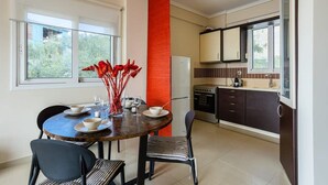 Une cuisine moderne avec un coin repas, comprenant une table ronde avec des chaises, un réfrigérateur et une fenêtre donnant sur un espace verdoyant.