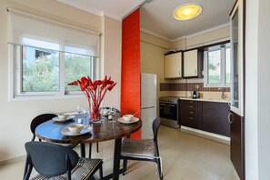 A modern kitchen with a dining area, featuring a round table with chairs, a refrigerator, and a window with a view of greenery. - Aigli Summer Getaway - Seaview Lux Retreat (Kalamata)