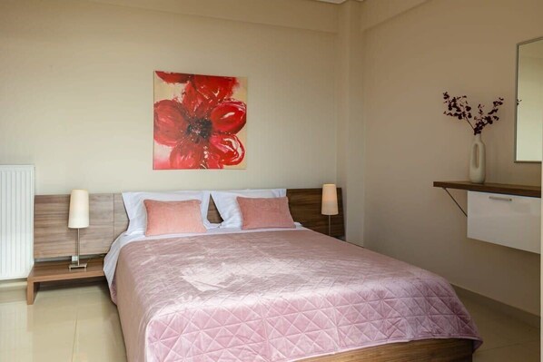 Habitación de hotel con cama, lámparas de noche, mesita de noche, estante con un florero y un cuadro floral grande.