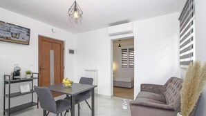 A modern living room with a sofa, a dining table with chairs, a coffee machine, and a plant.