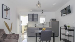 A modern kitchen with a dining area, a sofa, and a TV mounted on the wall.