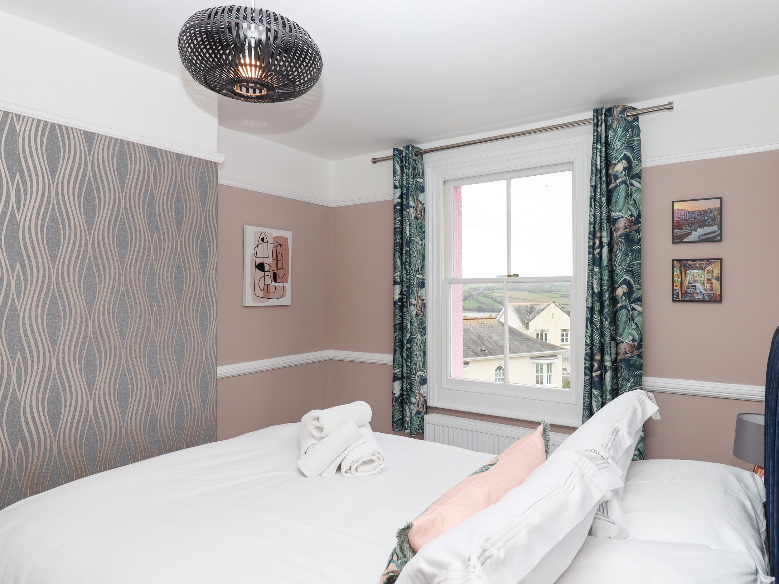 A bedroom with a bed, a window with curtains, a wall with a picture, and a hanging light fixture.
