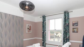 A bedroom with a bed, a window with curtains, a wall with a picture, and a hanging light fixture.