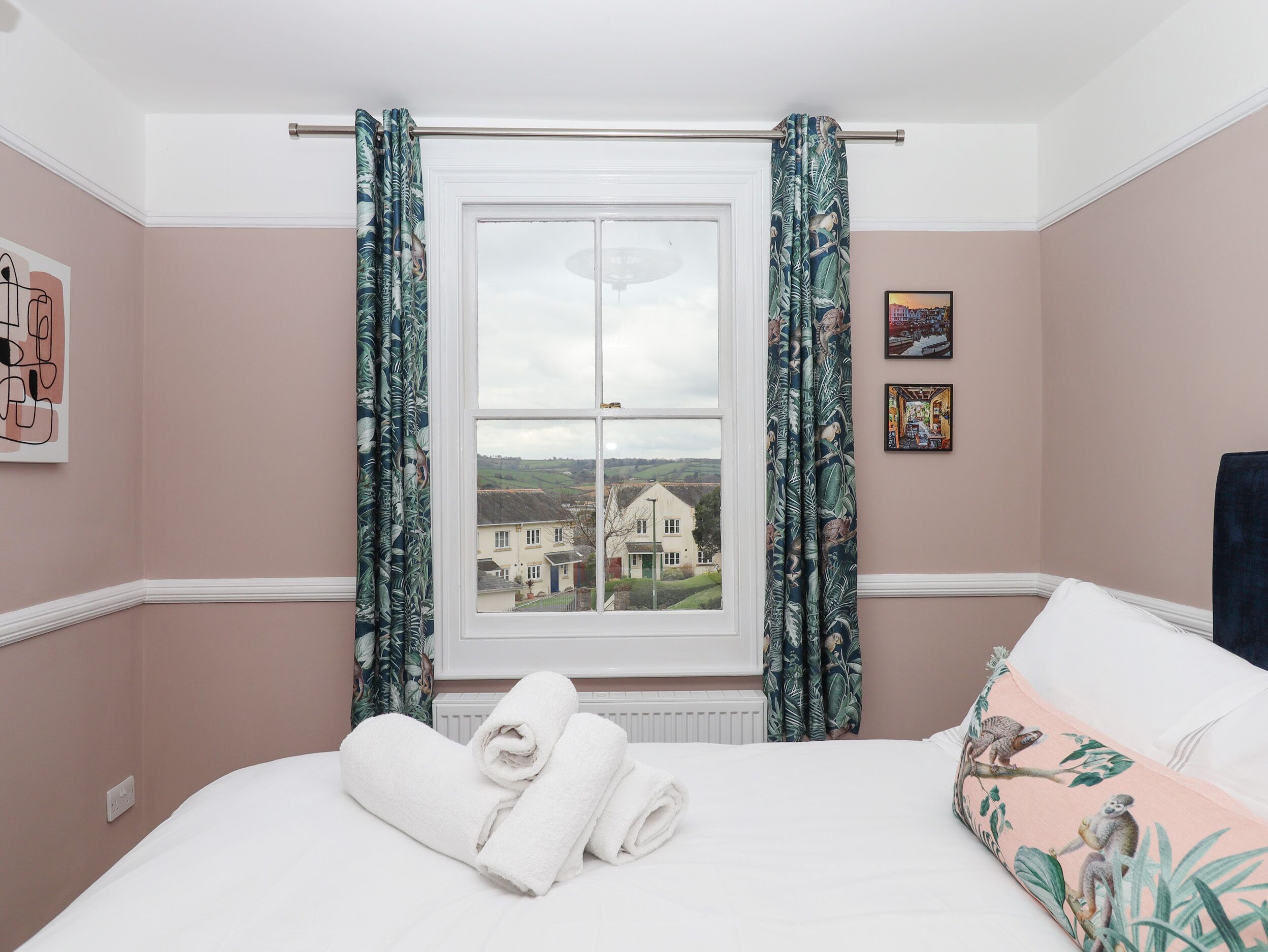 A hotel room with a large window, a bed with white linens, and a view of a house and fields.