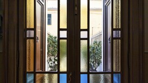 Vista a través de una ventana con marco de madera y múltiples cristales, que muestra un edificio con fachada amarilla y un árbol en el exterior.