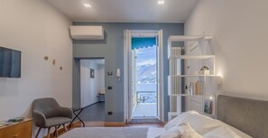A bedroom with a bed, a chair, a desk, a bookshelf, and a view of the sea through an open door.