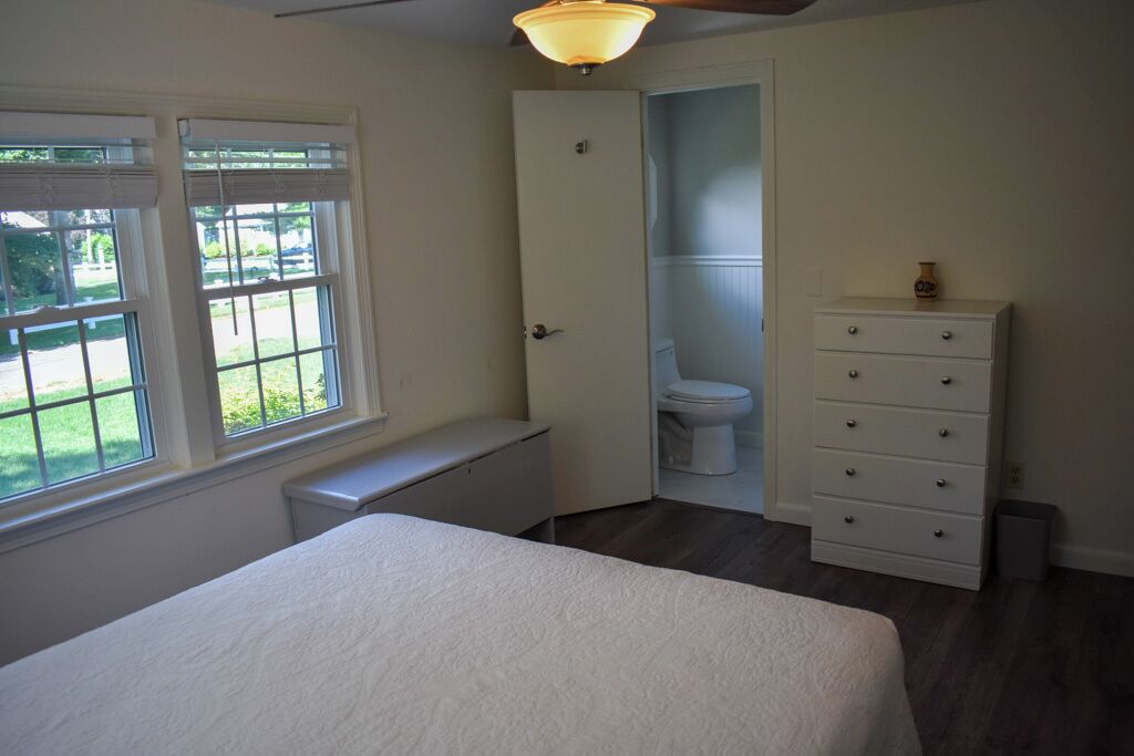 A bedroom with a bed, a dresser, a door leading to a bathroom, and a window with blinds.