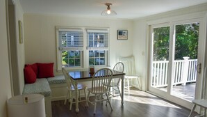 A dining area with a table and chairs, a bench with red cushions, and a view of the outdoors through large windows. - Renovated three bedroom home located in desirable Bayside Neighborhood! (Dennis)