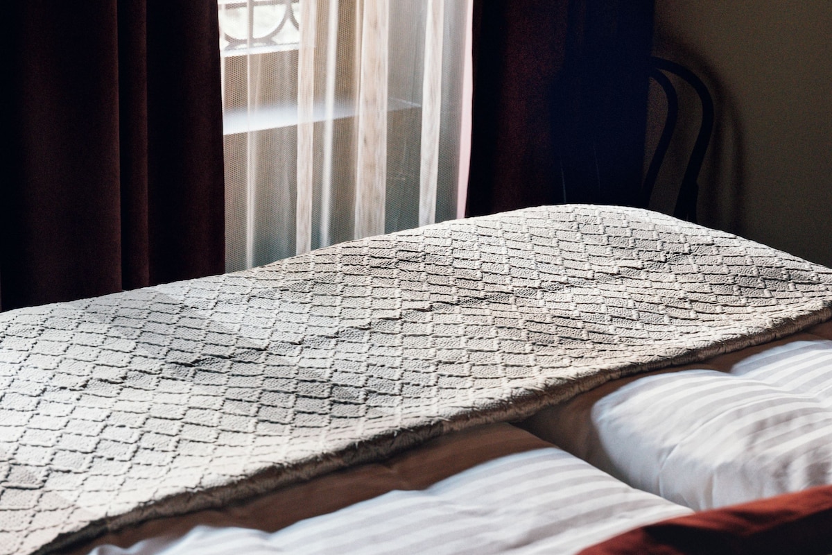 Un lit avec une couvre-lit à motifs, un oreiller blanc et une couverture rouge.
