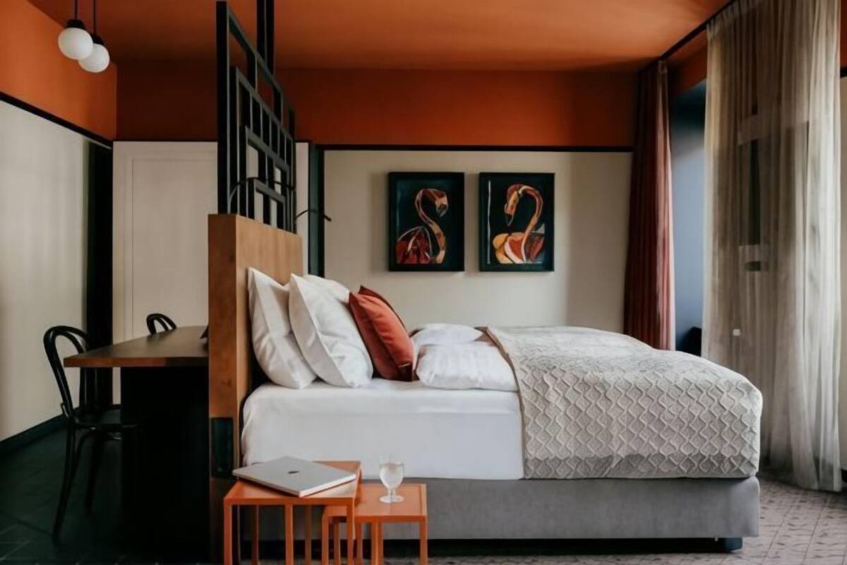 Een moderne hotelkamer met een bed, een bureau en twee abstracte schilderijen aan de muur.
