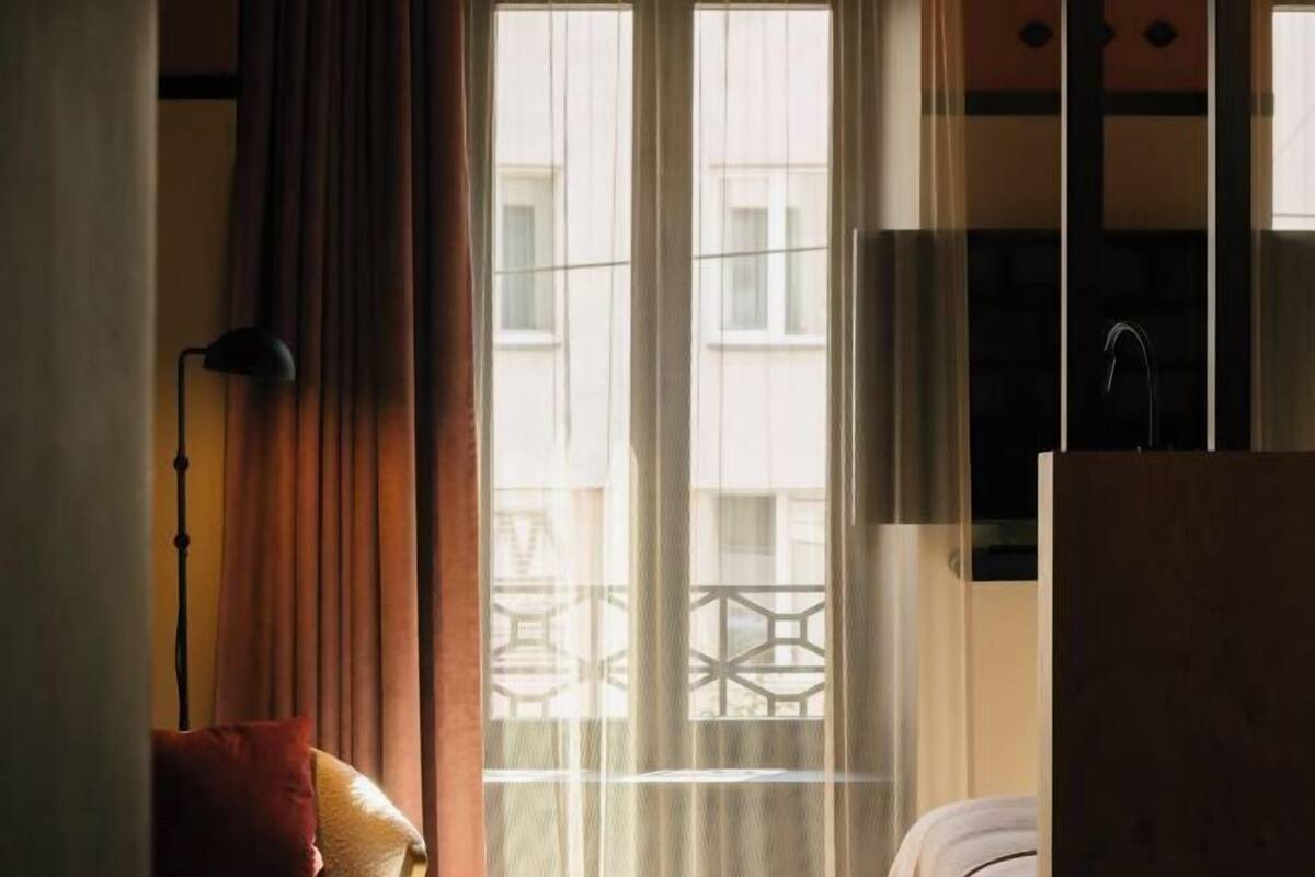Een kamer met een bed, een raam met gordijnen, een lamp en een televisie.