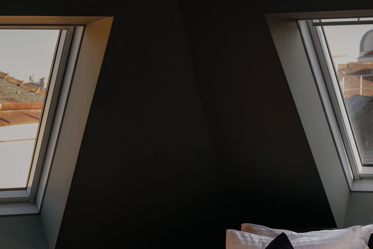 Een slaapkamer met dakraam, een bed met kussens en een nachtkastje met een kopje.