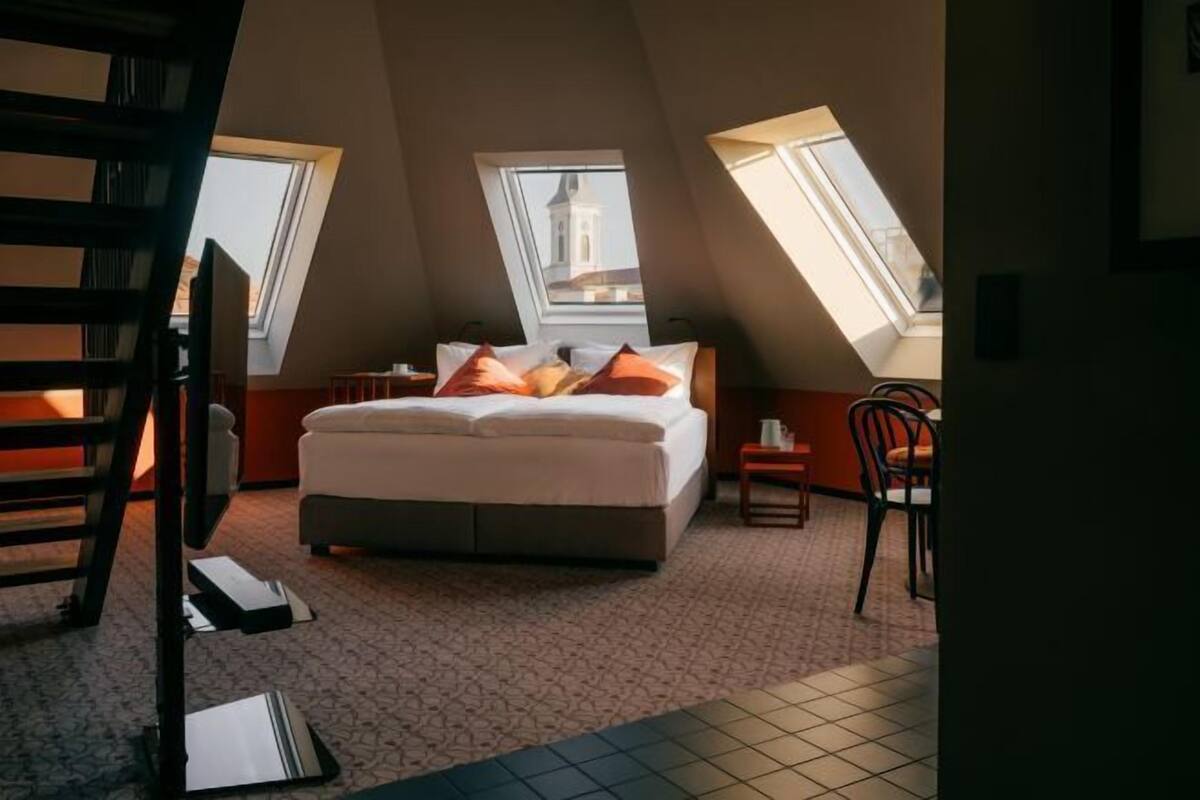 Een slaapkamer met een bed, twee nachtkastjes, een stoel en dakramen.