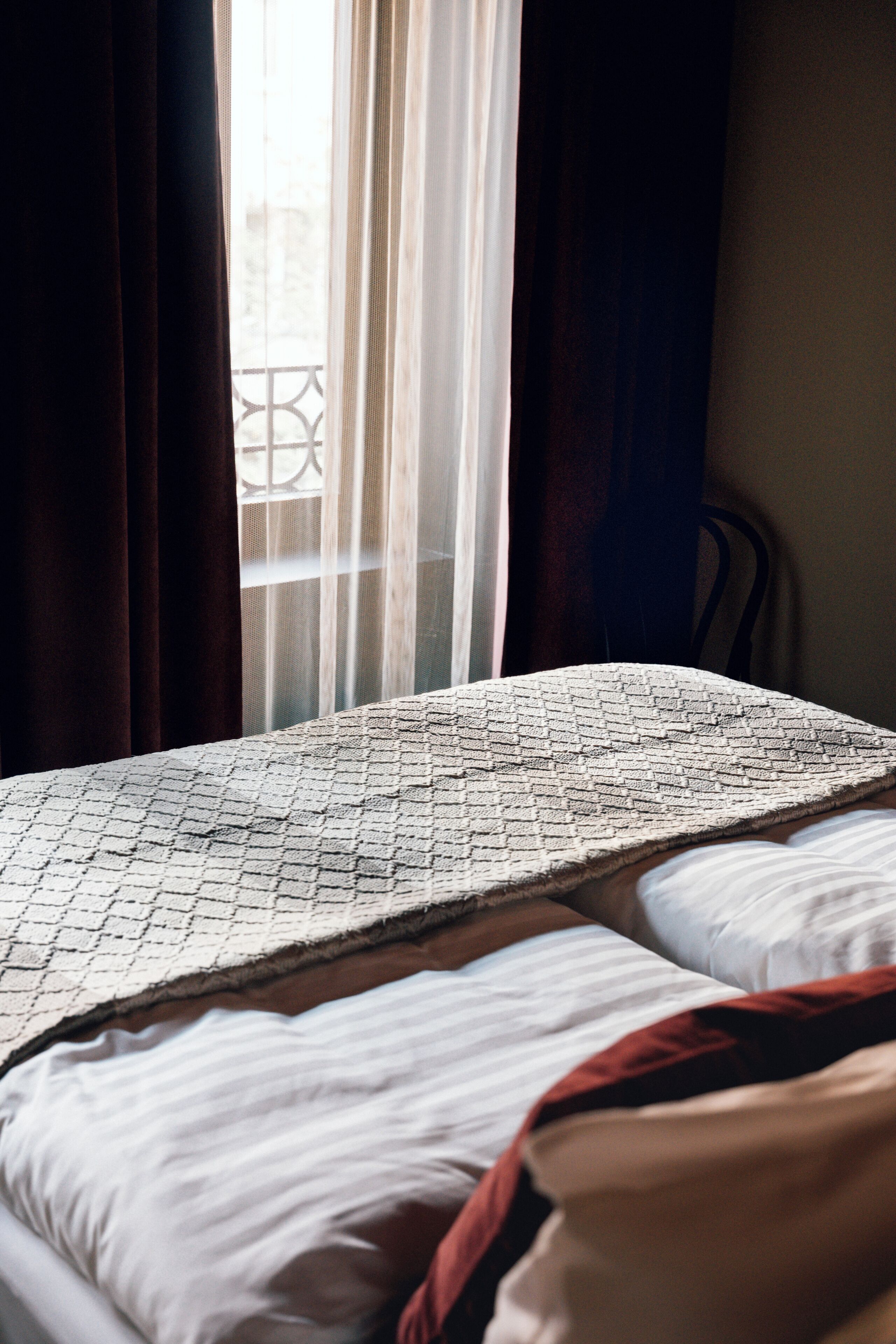 Un lit avec une couvre-lit à motifs, un oreiller blanc et une couverture rouge.