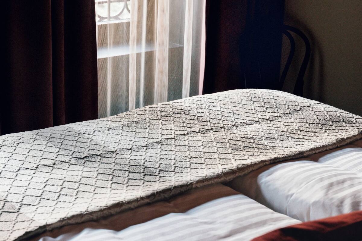 Een bed met een beddekleed met patroon, een wit kussen en een rode deken.