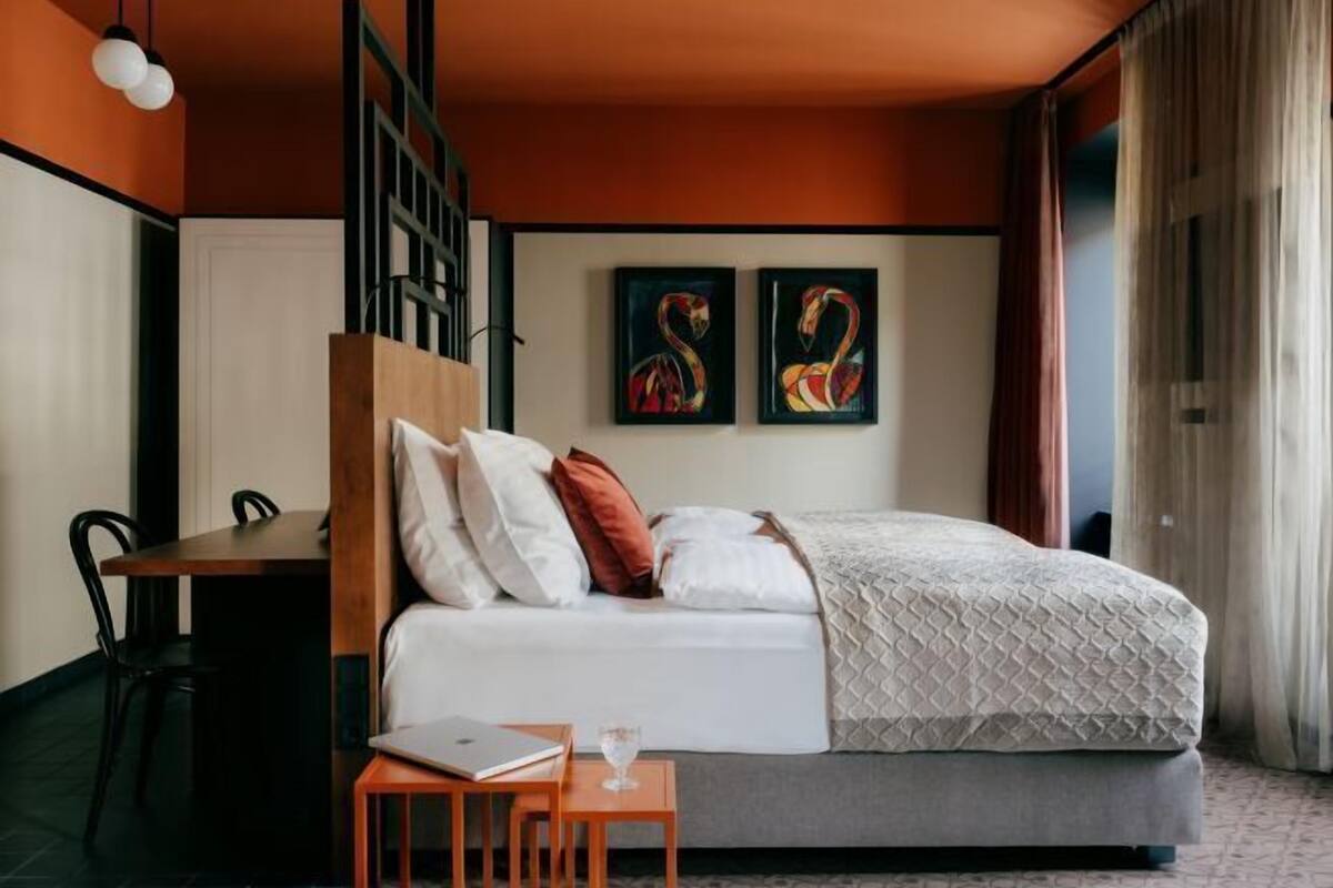 Een slaapkamer met een bed, een bureau en twee schilderijen aan de muur.