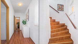 Un pasillo con piso de madera que conduce a una escalera con baldosas marrones.