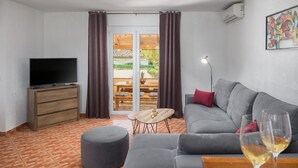 Una sala de estar moderna con un sofá gris, un televisor sobre un mueble de madera, una mesa de comedor con sillas y un ventanal corredero que da a un área exterior.