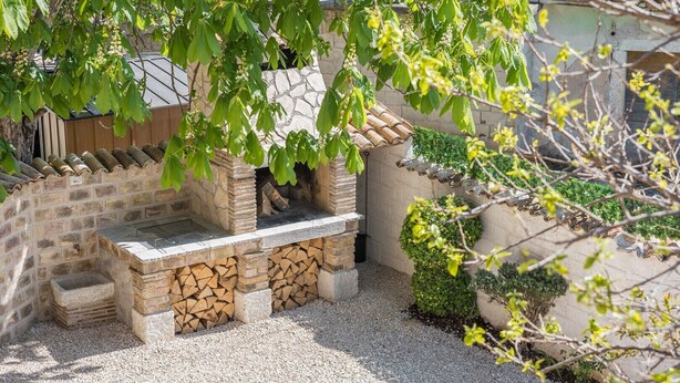 Zona de barbacoa de piedra con parrilla, rodeada de grava y pequeñas plantas.