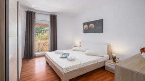 Un dormitorio moderno con una cama de madera, una mesita de noche con una lámpara y vistas al exterior a través de un ventanal grande.