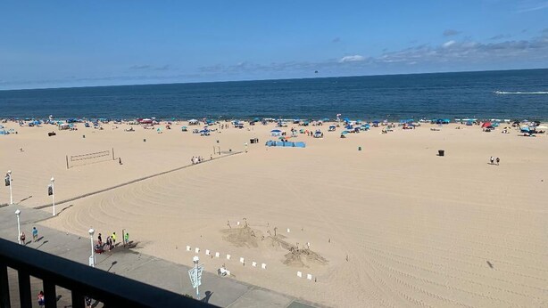 A beach with umbrellas and people, a volleyball net, and a clear sky. - Oceanfront Efficiency direct ocean views pool, gym & near all (Ocean City)