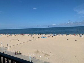 Ein Strand mit Sonnenschirmen, Menschen, einem Volleyballnetz und blauem Himmel.