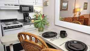 A compact kitchen with white cabinets, a stove, and a microwave. There is a dining area with a table, chairs, and a mirror reflecting the room. - Oceanfront Efficiency direct ocean views pool, gym & near all (Ocean City)