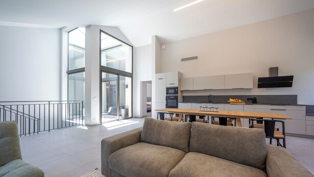 Een moderne woonkamer met een bank, een eettafel en een keuken met kasten en apparatuur.