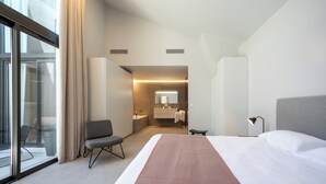 Een moderne hotelkamer met een groot bed, een bureau, een stoel, een badkamer met spiegel en uitzicht door een glazen deur.