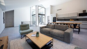 Een moderne woonkamer met een bank, een salontafel en een stoel. Er is een keukenhoek met kastjes en een eettafel.