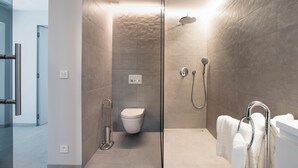 Een moderne badkamer met een glazen douchecabine, toilet en een bad met handdoekrek.