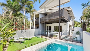 Une maison moderne à deux étages, dotée d’une piscine, d’un espace extérieur aménagé et d’une végétation luxuriante.