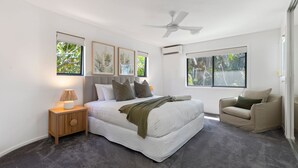 Une chambre avec un grand lit, une table de chevet, un ventilateur de plafond et une fenêtre donnant sur un paysage verdoyant.