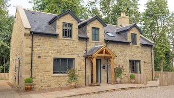 A stone house with a gabled roof, a wooden porch, and a gravel driveway.